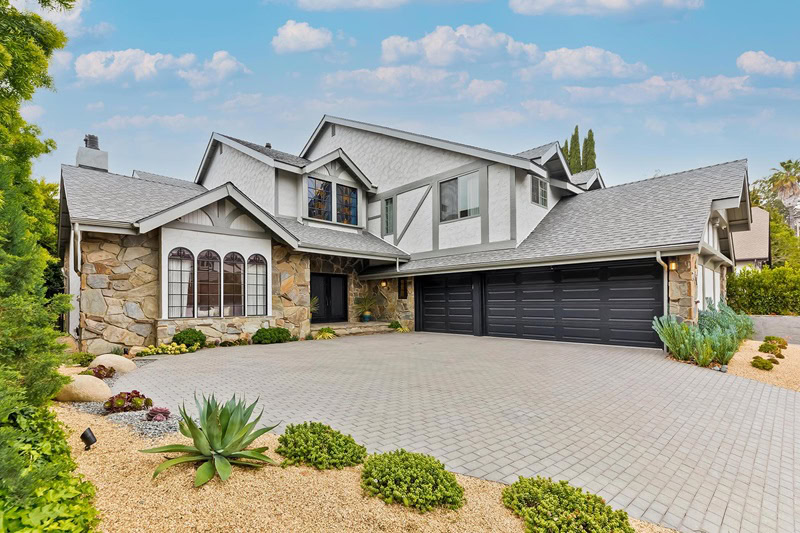 driveway in front of a two-story Tudor-style house with grey shingles and a black garage door