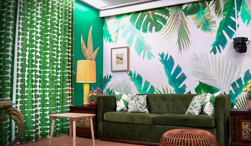 Bold interior from the set of season 6 of The Circle, with garden greens playfully used on the walls, curtains, and wallpaper with large painted leaves.