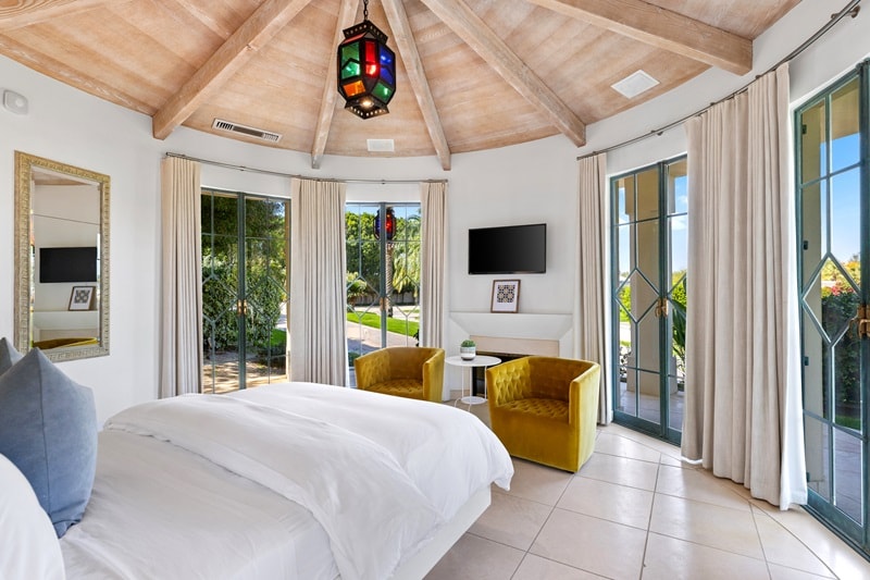 inside a bungalow guest pod on the Merv Griffin estate, featuring a domed wooden ceiling, a queen size bed, two armchairs and floor-to-ceiling windows