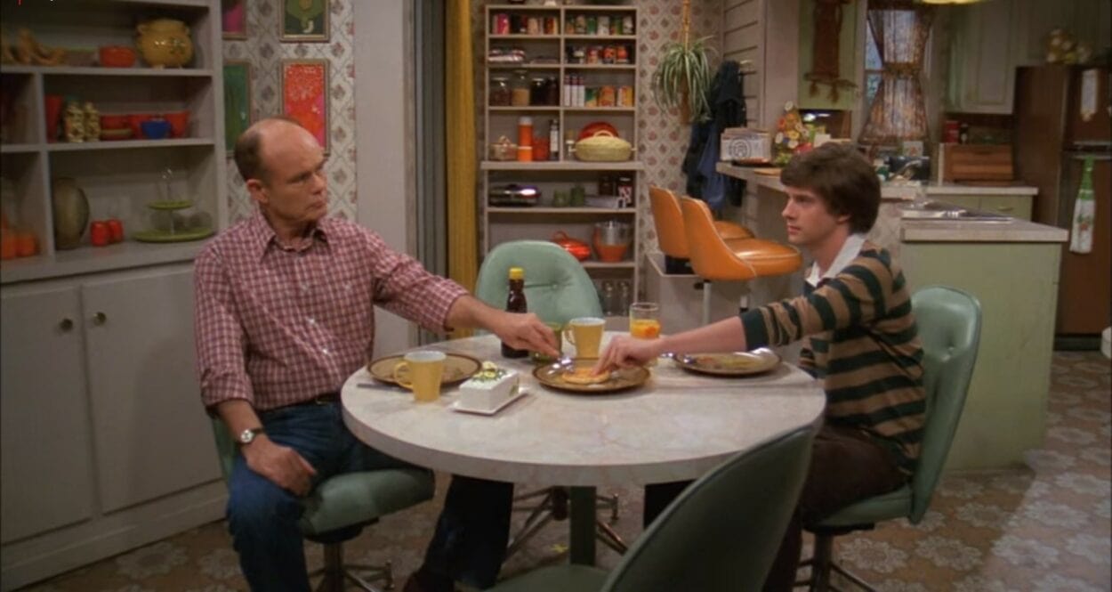 Inside the Forman house in That '70s Show, with actors Kurtwood Smith, Topher Grace sitting at the table, having breakfast and grabbing the last pancake.