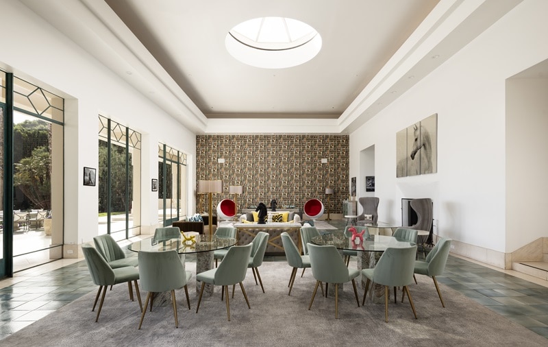 luxury living room with round skylight, patterned brown statement wall, two glass tables with chairs and a couch