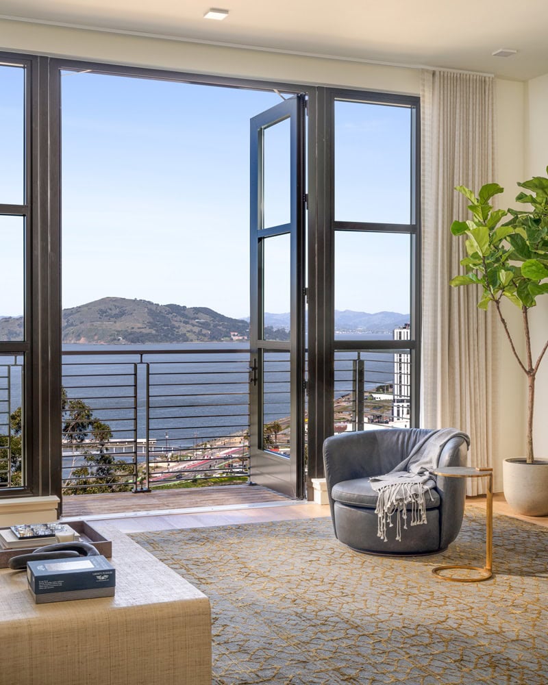 living room with an armchair and green plant, with the balcony doors opened and overlooking water views 