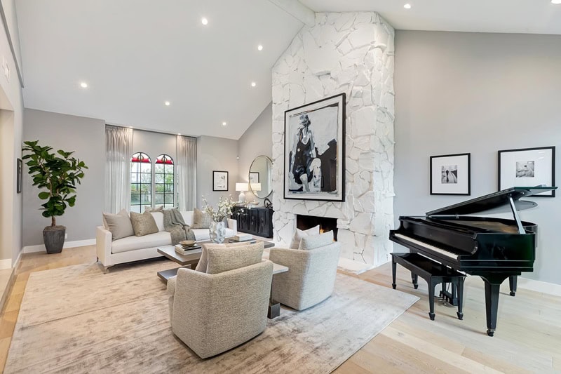 living room with white rock fireplace, sofa and two armchairs, and a piano