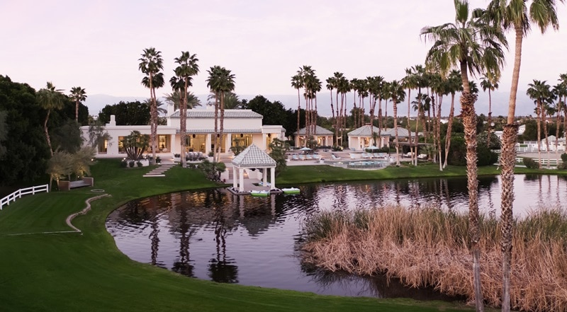 the main house on the property, a Moroccan-inspired luxury house seen from the backyard with lush lawns, lots of palm trees, and a man-made lake