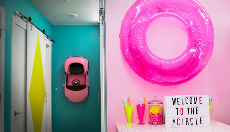 Colorful section of an apartment with one wall pink, the other bright teal, with decor items added for effect, like a pink round floatie and a pink toy car.