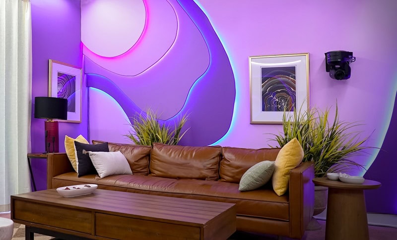 An eye-catching purple interior from one of the new apartments featured in The Circle, Season 6, with a brown leather couch sitting in front of a bright purple wall.