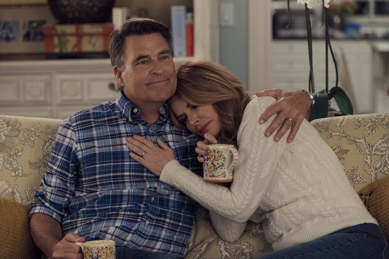 Roma Downey and Ted McGinley in a scene from The Baxters, holding each other in a caring embrace, while holding mugs in their hands.
