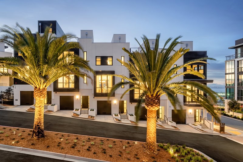 Architectural rendering showing the exterior of the two-story townhouses on Yerba Buena Island with modern exteriors and palm trees planted in front. 