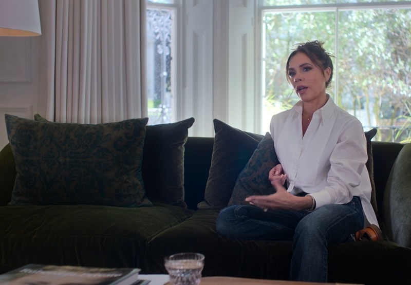 Victoria Beckham standing on a sofa in her living room, chatting with the Netflix crew for her documentary, "Beckham"