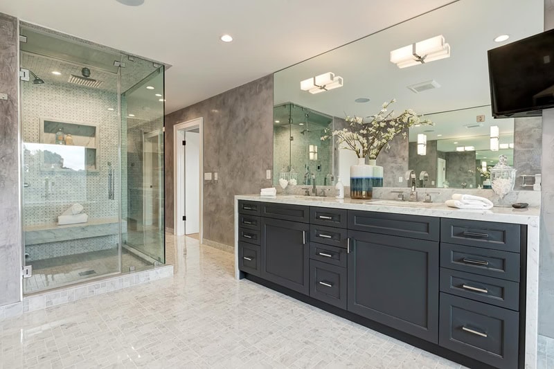 Bathroom vanity with black cabinets and large mirror next to a walk-in glass shower
