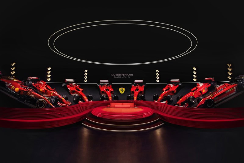 A large red bed set in a middle of a Ferrari showroom, with red racing cars surround it 