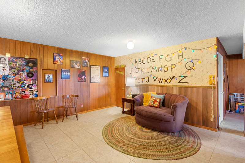 basement recreational area with a round swivel armchair, wood paneling, and the Stranger Things alphabet on the wall. 