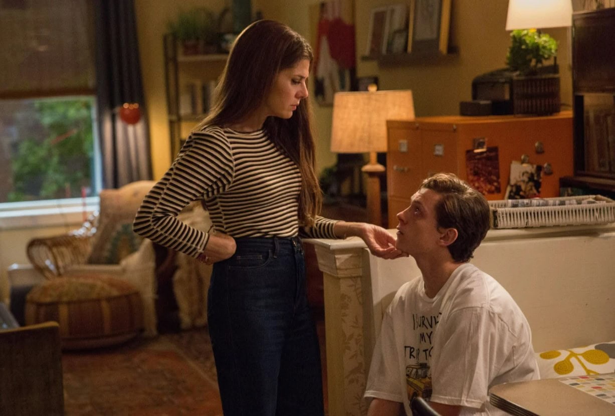 Marisa Tomei as Aunt May and Tom Holland as Peter Parker in a "Spiderman" scene showing the two characters inside their apartment, talking, with Marisa gently touching Tom's chin. 