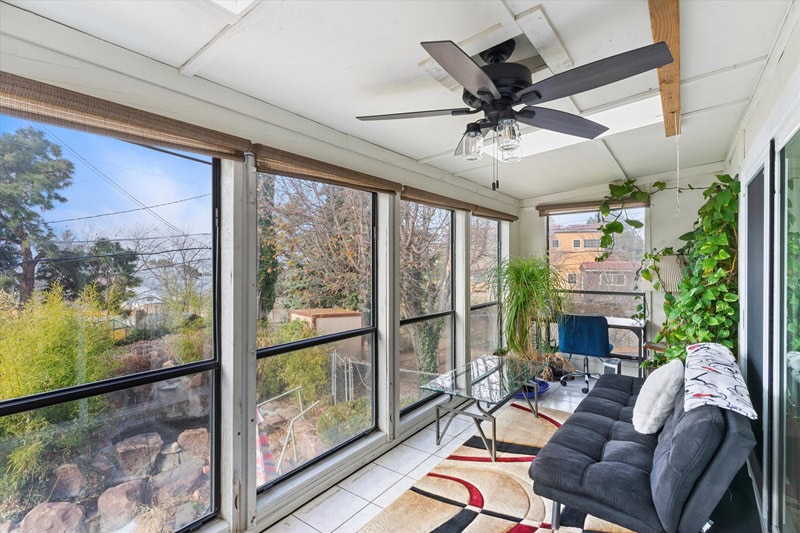 Closed balcony with a futon, glass table, small desk in the far corner, and a ceiling fan. 