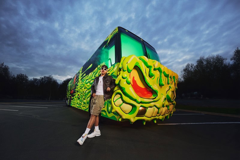 reggaeton superstar Feid leaning on his green tour bus covered in plastic slime with green smoke coming out from the cabin. 