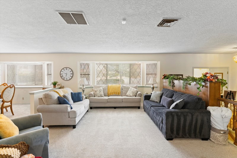 living area in an Albuquerque house with 3 sofas, plush carpeting throughout ad large windows behind the sofa. 