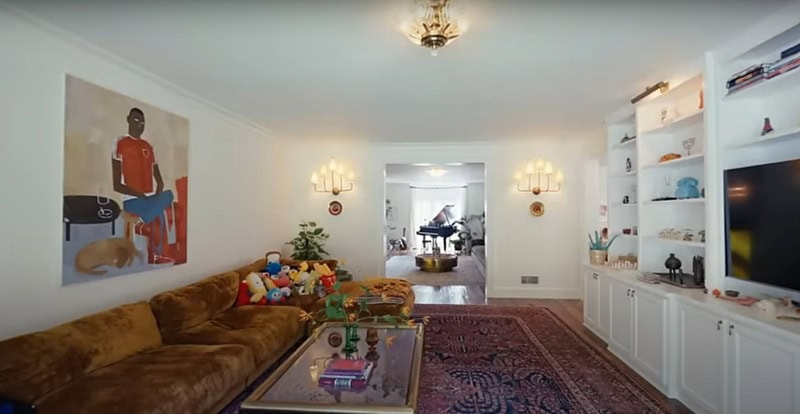 living room with a painting, a large sofa full of colorful plushies, and white furniture covering one wall.