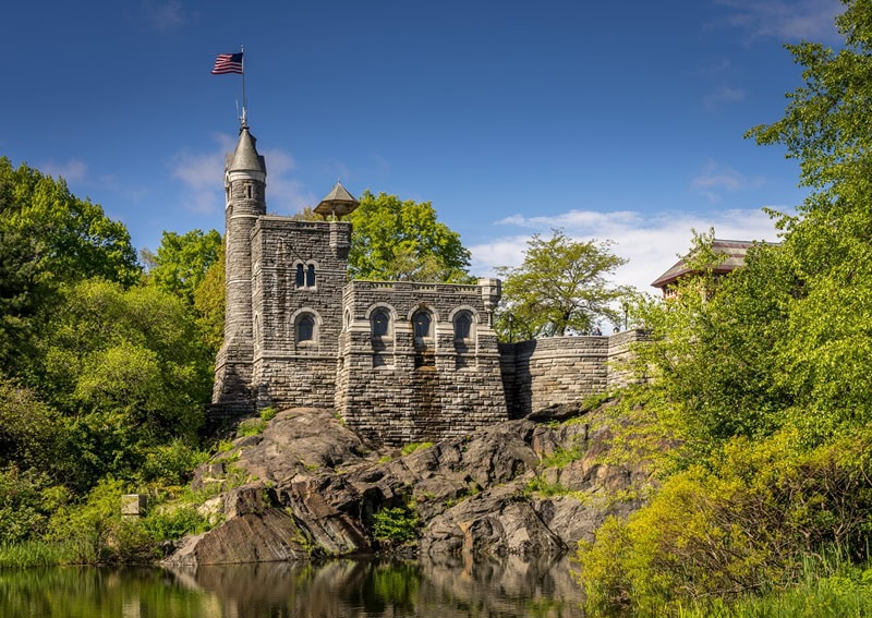 closeup on the tower of the castle, emerging from a green and rocky landscape, and sporting an American flag at the top. 