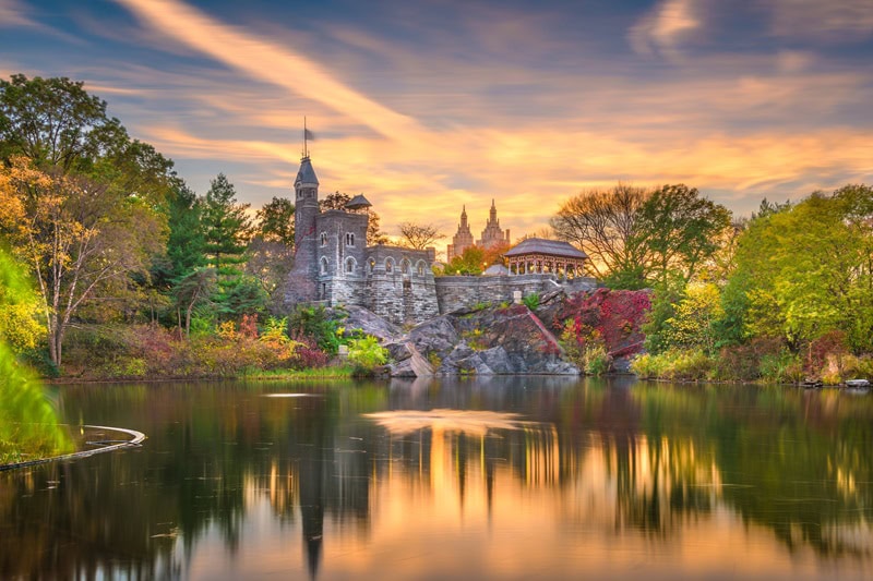 a painting-like picture of the Belvedere Castle, taken from across the pond and showing the structure surrounded by very vibrant fall colors and foliage. 