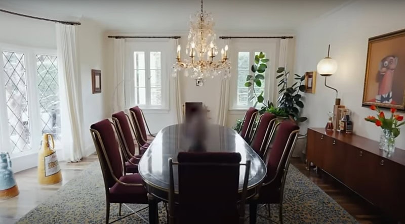 Formal dining room with tufted dark red velvet chairs, and oval dining table, and a crystal chandelier hanging above.