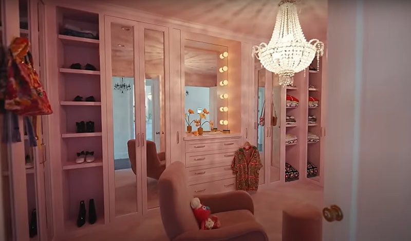 the color-changing closet set to pink hues, with open shoe and clothes cabinets in view, surrounded by mirrors and with a large crystals chandelier in the middle.