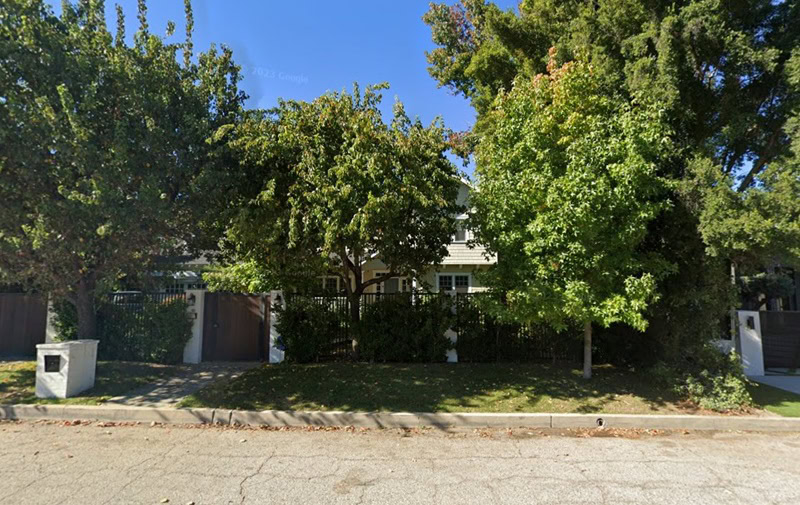 a two-story suburban home hidden behind thick trees, barely visible from the street