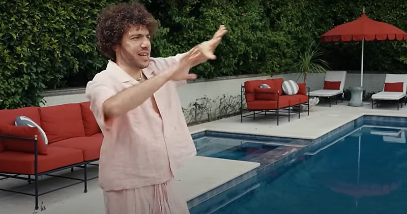 Benny Blanco next to his pool, gesticulating, with the pool, spa, and lounging chairs in view.